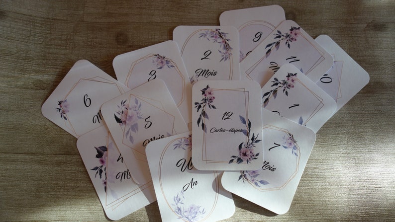 May include: A set of 12 cards with floral designs and gold accents. The cards are numbered 1 through 12, with the number 12 labeled "Cartes-aper". The cards also include the words "Mois" and "An".