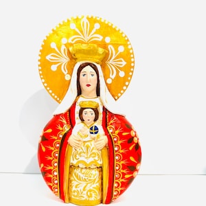 Może przedstawiać: Ręcznie malowana drewniana figurka Matki Boskiej z Dzieciątkiem Jezus. Figurka jest pomalowana na czerwono, złoto i biało z złotą aureolą wokół głowy Maryi.