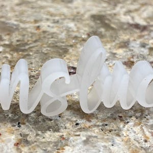 May include: A three-dimensional white plastic sign featuring the word Translucent in a cursive script font. The letters are connected and have a smooth, matte finish, standing upright with a semi-transparent appearance throughout the structure.