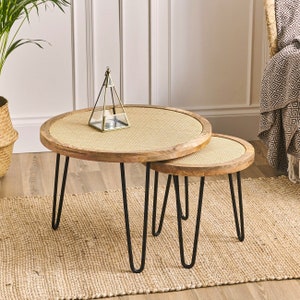 May include: A set of two round wooden nesting tables with black hairpin legs. The tabletops are woven with a light brown rattan pattern.