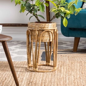 Peut inclure: Un support de plante en osier naturel avec une base ronde et quatre pieds. Une plante en pot avec des fleurs blanches est posée sur le support. Le support est sur un tapis tissé.