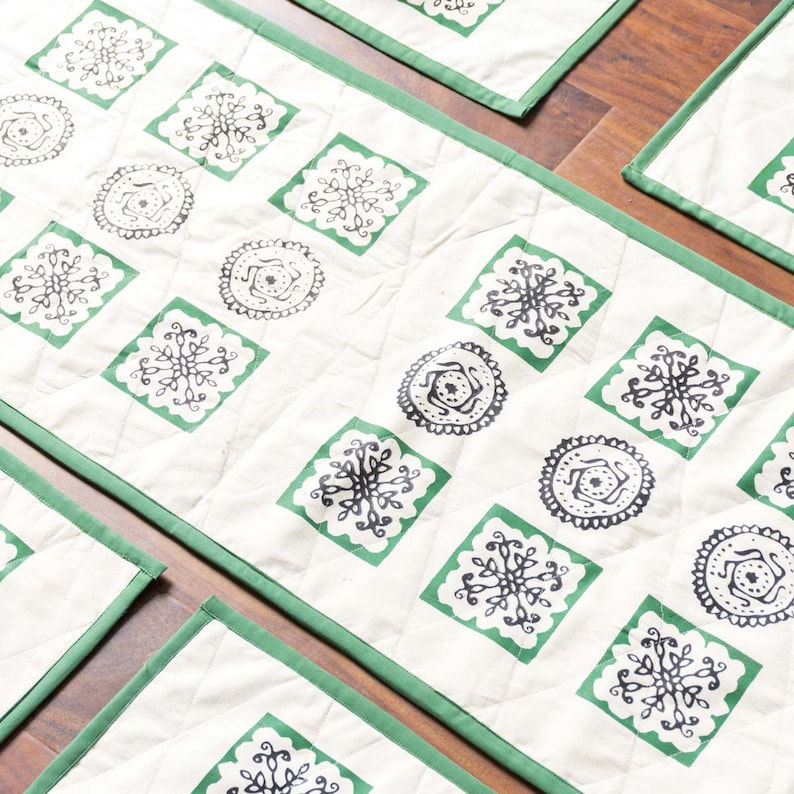 long handmade table cloth with block print with four matching placemats. With black block print in patterned round and square shapes with green accents. The beige thick fabric is framed with a green edge. The table runner and placemats are reversible