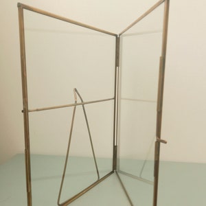 May include: A gold-toned metal picture frame with a glass front and a stand. The frame is open and the stand is visible.