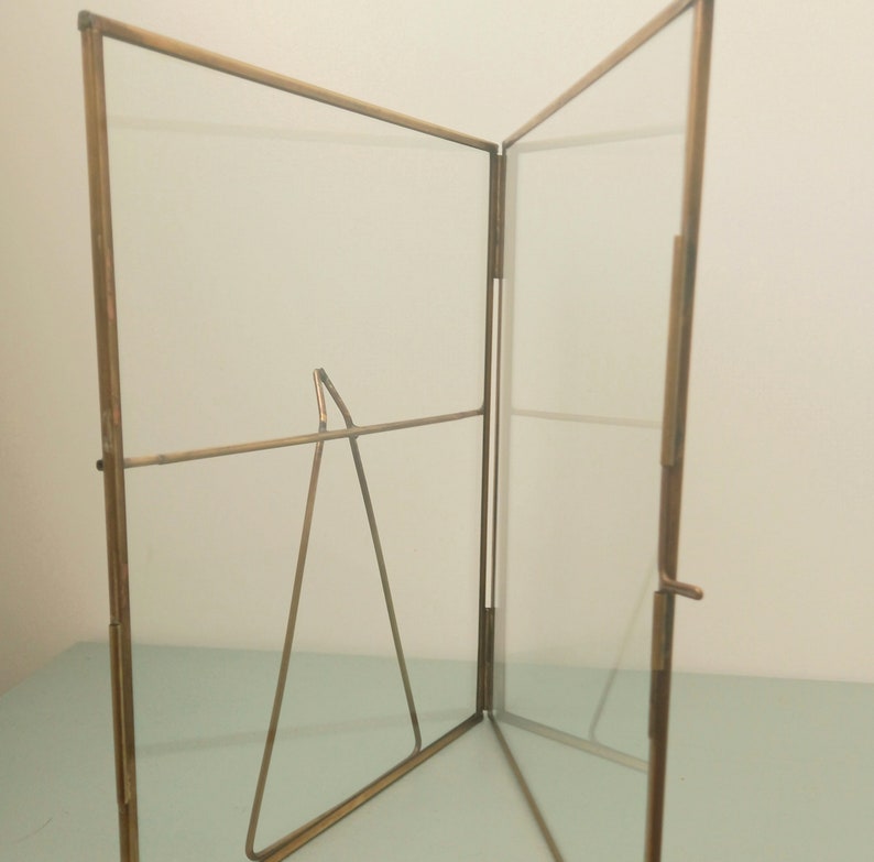 May include: A gold-toned metal picture frame with a glass front and a stand. The frame is open and the stand is visible.