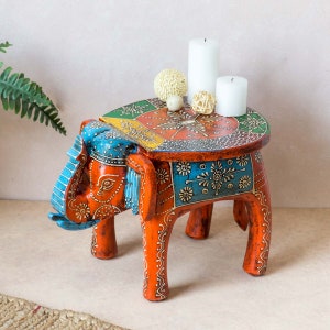 May include: A colourful wooden elephant stool with intricate hand-painted details. The stool has a round top and four legs, and is decorated with a variety of floral and geometric patterns in shades of red, orange, blue, green, and yellow.