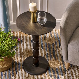 May include: A dark wood round side table with a turned pedestal base. The table is decorated with a white candle and a glass of water.