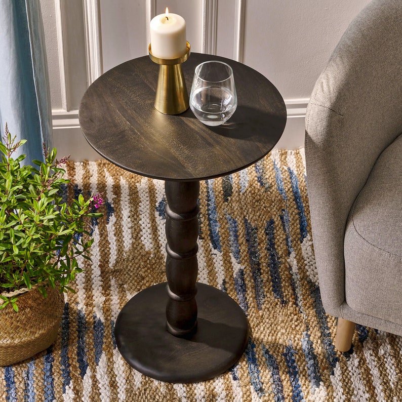 May include: A dark wood round side table with a turned pedestal base. The table is decorated with a white candle and a glass of water.