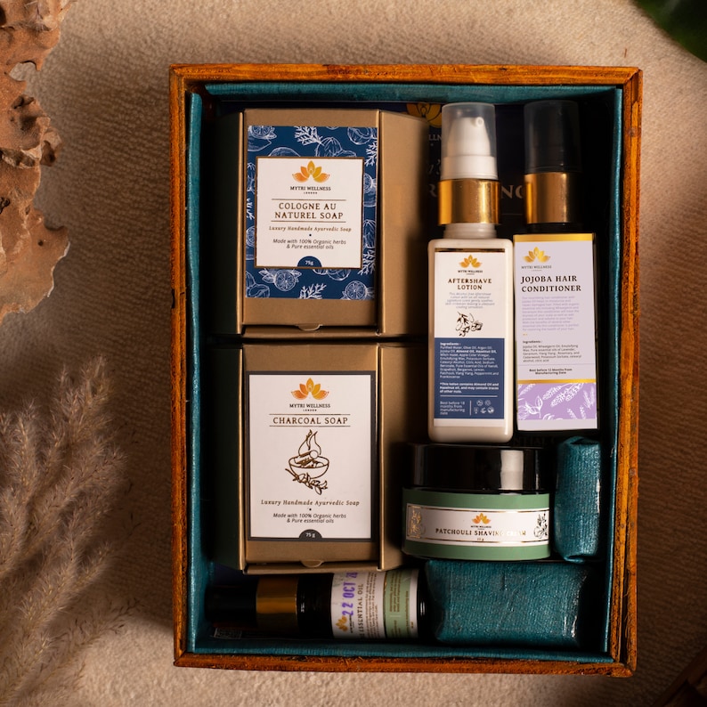 Puede incluir: Una caja de madera llena de productos de ba&ntilde;o y cuerpo. La caja contiene dos barras de jab&oacute;n, una etiquetada como "Cologne au Naturel Soap" y la otra como "Charcoal Soap". Tambi&eacute;n hay una botella de loci&oacute;n para despu&eacute;s del afeitado, una botella de acondicionador para el cabello de jojoba, un tarro de crema de afeitar de pachul&iacute; y una peque&ntilde;a botella de aceite esencial.