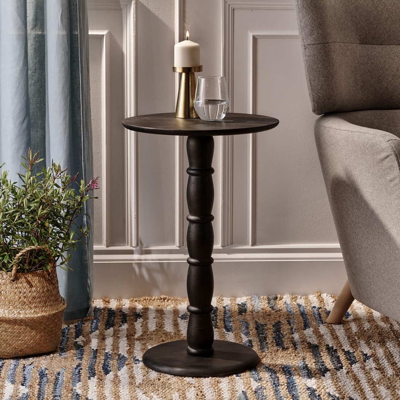 May include: A black wooden side table with a round top and a turned pedestal base. The table is decorated with a candle and a glass on top.