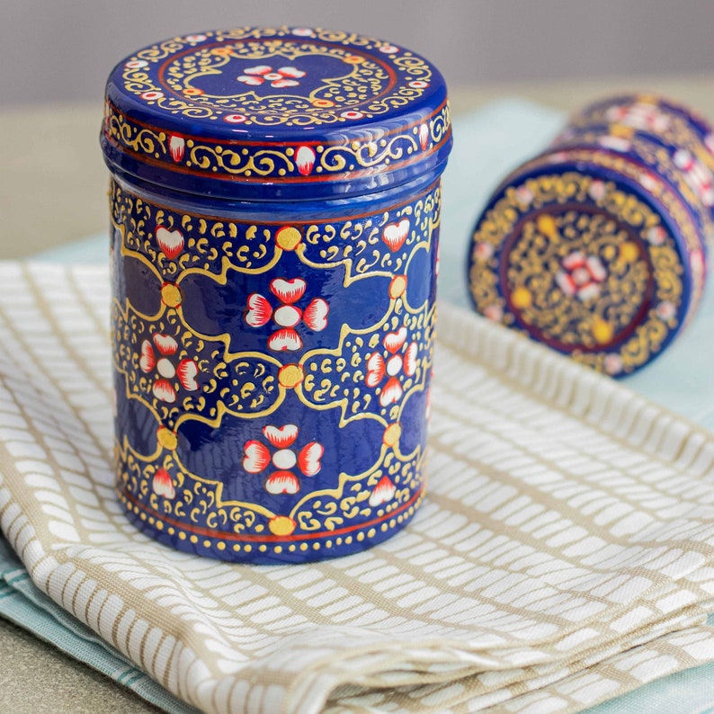 Steel kitchen containers coated with enamal and handpainted with an ornamental flower pattern. These nesting boxes with lid are suitable for food or small items and come in dark blue, green and red.