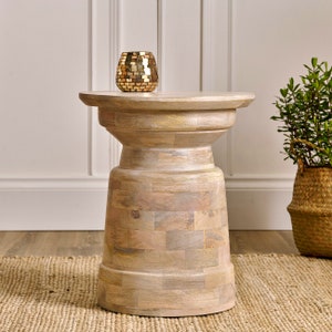 May include: A whitewashed wooden side table with a round top and a pedestal base. The table has a distressed finish and is made of natural wood.