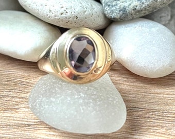 May include: A gold ring with a large, oval-shaped, purple gemstone set in a bezel setting.