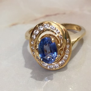 May include: A gold ring with a blue oval sapphire surrounded by a halo of smaller diamonds.