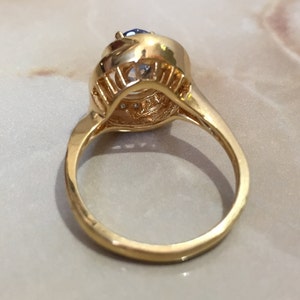 May include: A gold ring with a large blue gemstone surrounded by smaller clear gemstones.