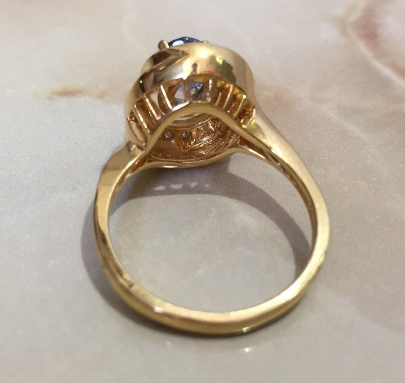 May include: A gold ring with a large blue gemstone surrounded by smaller clear gemstones.