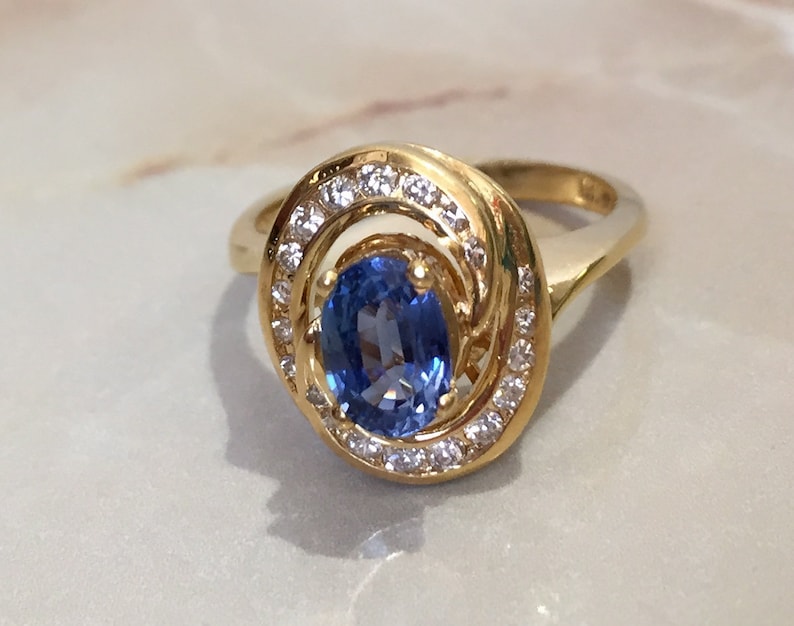 May include: A gold ring with a blue oval sapphire surrounded by a halo of smaller diamonds.