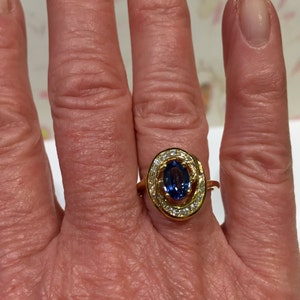 May include: A gold ring with a blue oval gemstone surrounded by smaller diamonds. The ring is set in a twisted band.
