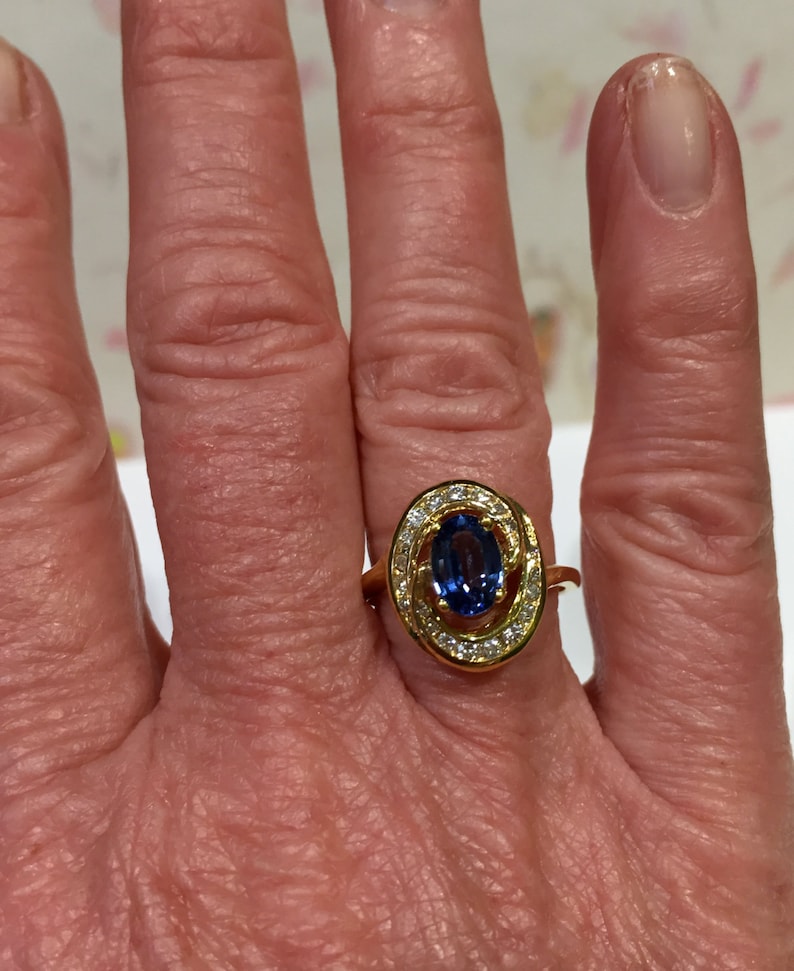 May include: A gold ring with a blue oval gemstone surrounded by smaller diamonds. The ring is set in a twisted band.
