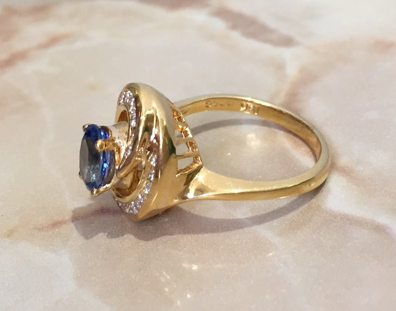 May include: A gold ring with a blue gemstone surrounded by smaller clear gemstones. The ring has a twisted band.