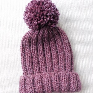 May include: A purple knitted beanie with a fluffy pom pom on top.