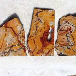 May include: Three pieces of polished agate with a swirling pattern of brown, orange, and white. The agate is a natural stone with a unique and beautiful pattern.