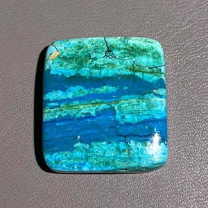 May include: A rectangular polished gemstone cabochon featuring horizontal bands of vibrant turquoise, deep royal blue, and forest green with dark natural veining throughout the surface, showcasing a smooth, glossy finish and rounded corners.