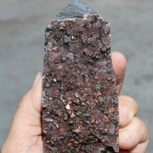 May include: A dark gray and brown crystal point with a rough, textured surface. The crystal is covered in small, sparkling crystals.