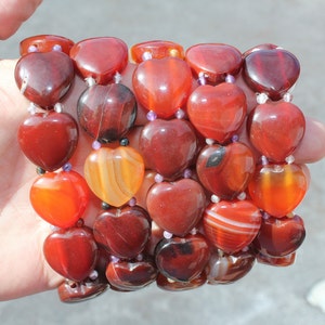 May include: A strand of heart-shaped carnelian beads in shades of red, orange, and brown. The beads are strung on a clear elastic cord.