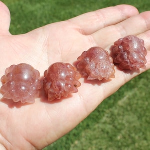 May include: Four small, pink, crystal octopus figurines. The octopus figurines are carved from a translucent pink crystal with a sparkly finish.