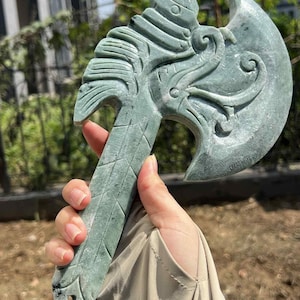 May include: A hand-carved, green stone axe with intricate details. The axe head features a curved blade and ornate carvings, while the handle has a textured, diamond-patterned design. The overall aesthetic suggests a historical or fantasy theme.