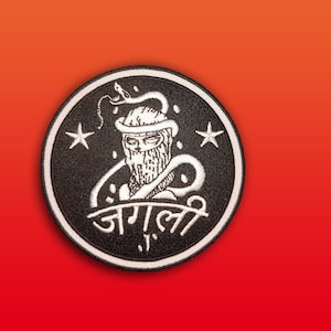 May include: Black and white embroidered patch with a hooded figure, a snake, and two stars. The text "जगली" is written below the figure.