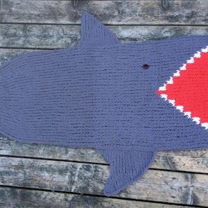 May include: A grey knitted shark blanket with a red and white open mouth.