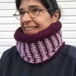 May include: A handmade crochet cowl in shades of purple and pink. The cowl features a textured stitch pattern with a fluffy, faux fur trim around the neck. This cozy neck warmer is perfect for cold weather.