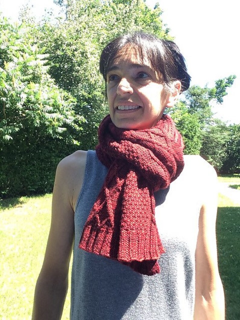 Puede incluir: Una mujer con una camisa gris sin mangas y una bufanda de punto roja alrededor del cuello. La bufanda es de punto de cable.