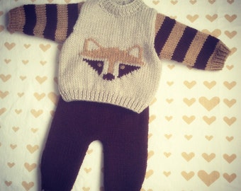 May include: A knitted baby outfit with a brown and beige striped sweater featuring a raccoon face and brown pants.