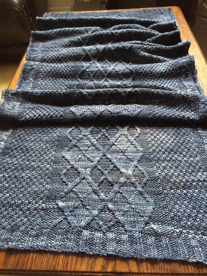 Puede incluir: Una bufanda de punto azul con un patr&oacute;n de diamantes. La bufanda est&aacute; doblada por la mitad y tiene una superficie texturizada.