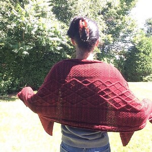 Puede incluir: Una mujer lleva un c&aacute;rdigan de punto granate con un patr&oacute;n de rombos. El c&aacute;rdigan est&aacute; drapeado sobre sus hombros y lleva pantalones cortos de mezclilla.