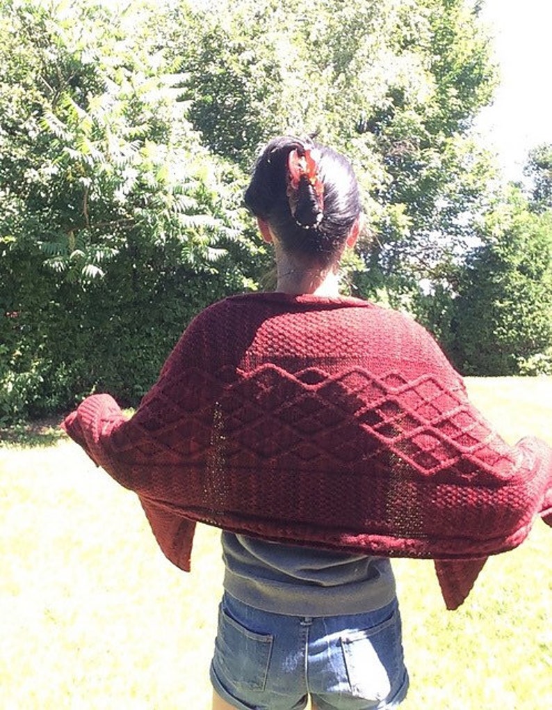 Puede incluir: Una mujer lleva un c&aacute;rdigan de punto granate con un patr&oacute;n de rombos. El c&aacute;rdigan est&aacute; drapeado sobre sus hombros y lleva pantalones cortos de mezclilla.