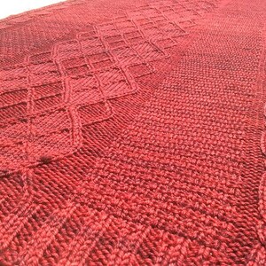 Puede incluir: Un chal de punto rojo con un patr&oacute;n de diamantes y un borde de cable.