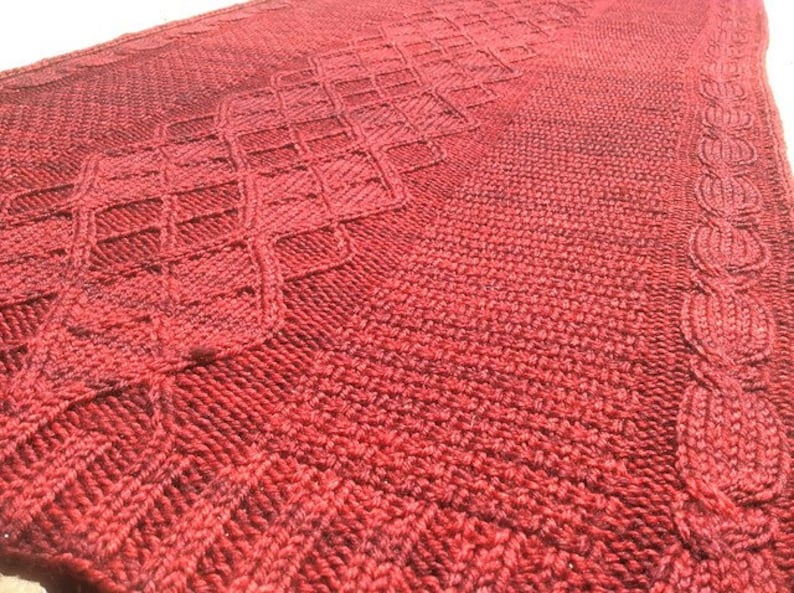 Puede incluir: Un chal de punto rojo con un patr&oacute;n de diamantes y un borde de cable.