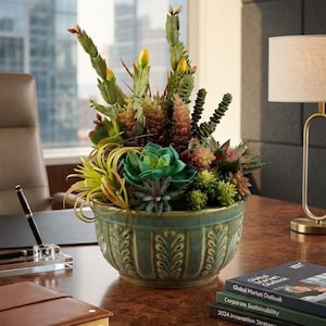 May include: A decorative green ceramic bowl with a vertical ribbed pattern containing an arrangement of various artificial succulents and cacti in shades of green, yellow, and reddish-brown, featuring tall spiky stems and rounded rosettes.