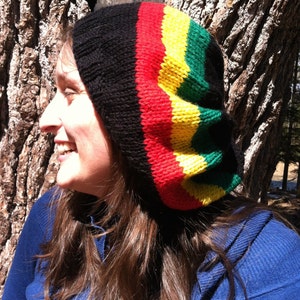 May include: A woman wearing a black, red, yellow and green knitted beanie hat. The hat has a striped pattern.