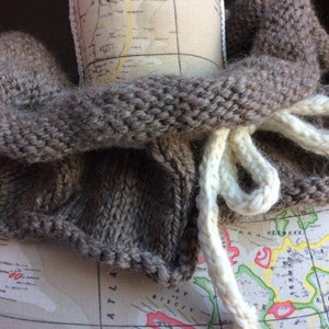 May include: A brown knitted cowl with a white knitted cord. The cowl is folded and draped over a map.