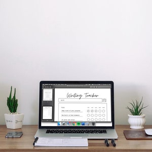 May include: A laptop displays a "Writing Tracker" document on a wooden desk. The desk also holds speakers, a watch, a phone, a mouse, and potted plants. The tracker has sections for dates and progress tracking. The background is a plain white wall.