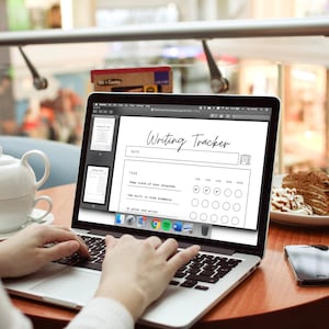May include: A laptop displaying a "Writing Tracker" template, with a teapot and cake on a table. The screen shows a progress chart with checkboxes. The text "Writing Tracker" is at the top. A smartphone sits on the table.