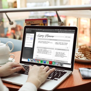 May include: A person using a laptop with an "Essay Planner" displayed on the screen. A white teapot and cup sit on the table, along with a slice of cake and a smartphone. The laptop screen shows a writing template.