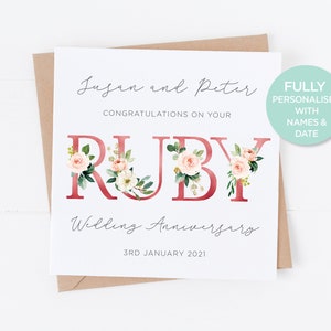 May include: A white greeting card with the words "Jusan and Peter" and "Congratulations on your Ruby Wedding Anniversary" in elegant script. The word "RUBY" is in a bold, red font, decorated with floral arrangements. The date "3rd January 2021" is also included.