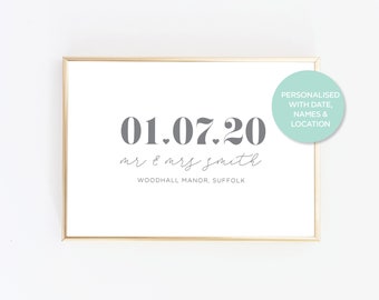 May include: A rectangular print in a gold frame featuring the date 01.07.20 in large grey font, the text mr & mrs smith in a cursive script, and the location text WOODHALL MANOR, SUFFOLK. A circular teal sticker reads PERSONALISED WITH DATE, NAMES & LOCATION.
