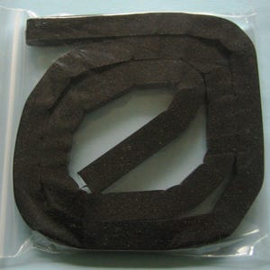 May include: A coiled, black foam weatherstrip is sealed inside a clear plastic bag. The weatherstrip is rectangular with a textured surface. The foam appears to be flexible and is designed to seal gaps.