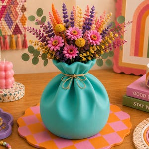 May include: A turquoise vase with a cinched neck tied with a thin twine string, filled with a vibrant arrangement of dried flowers including pink daisies, yellow billy balls, purple lavender, and green eucalyptus stems.